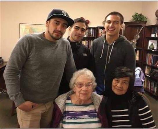 Four men and two older women gather happily in a warm indoor space, showcasing family ties.