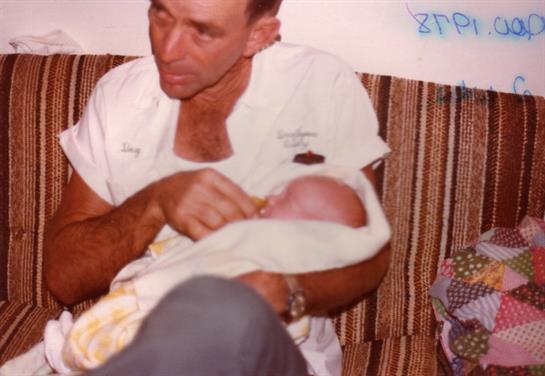 A grandfather lovingly cradles a newborn in a living room, surrounded by warmth and family love.