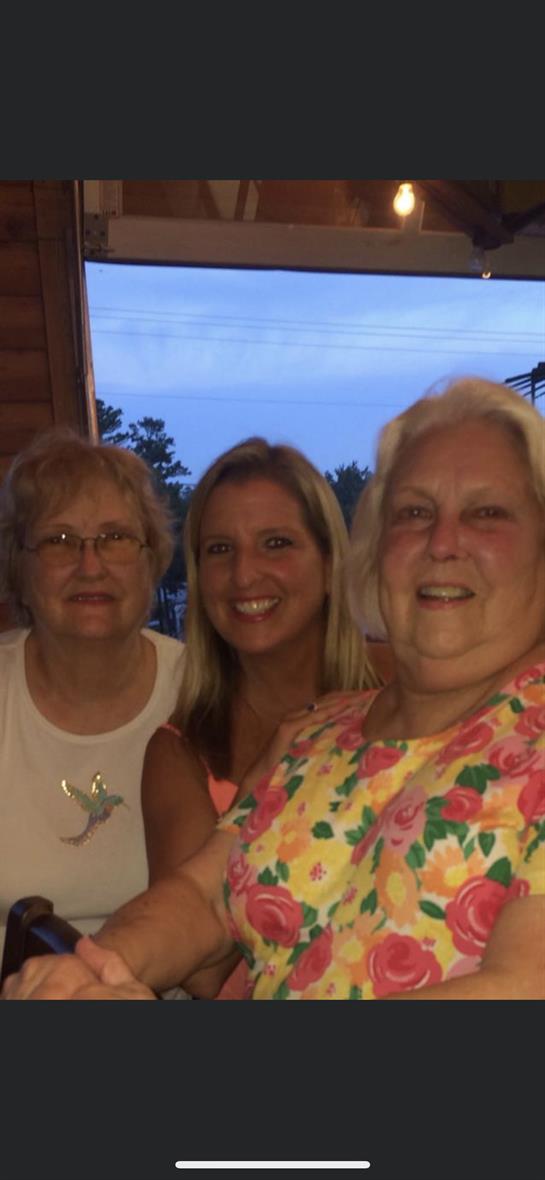 Three women smile warmly together, enjoying each other's company on a summer evening.
