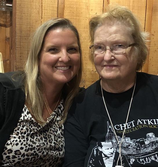 Two women are sharing smiles while seated together in a warm wooden room.