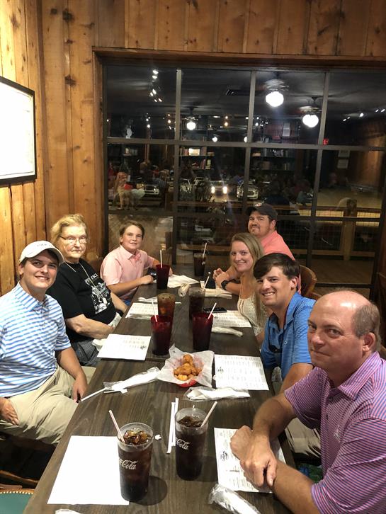 A group of seven family members sits at a table, sharing dinner and engaging in conversation.