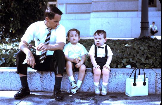 A father enjoys a relaxed moment with his two young children on a sunny day in the park.