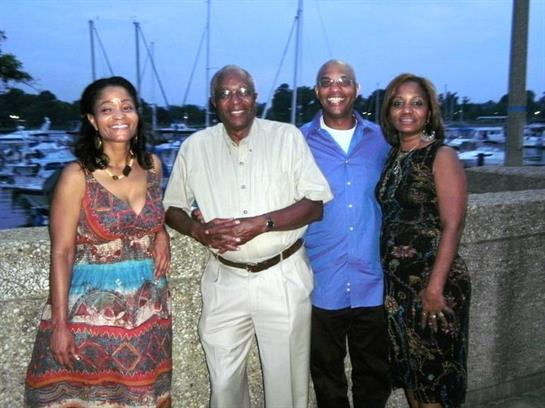 Four family members pose together at a marina near sunset, capturing a joyful moment.