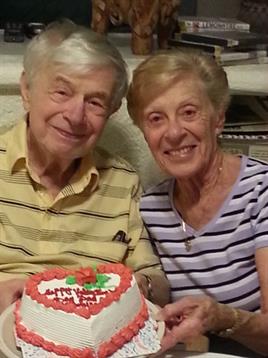 A happy couple smiles together while celebrating their anniversary with a cake at home.