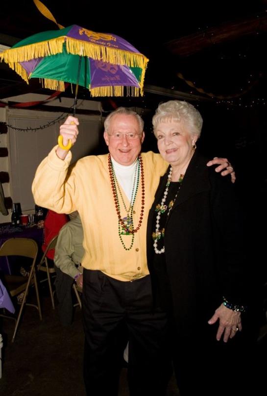 An older couple celebrates joyfully at a vibrant party while holding a decorated umbrella.