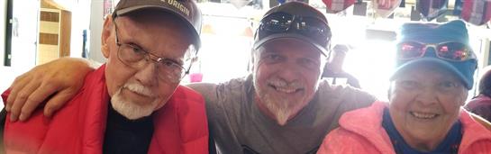 Two men share a friendly moment while smiling and sitting in a lively social setting.