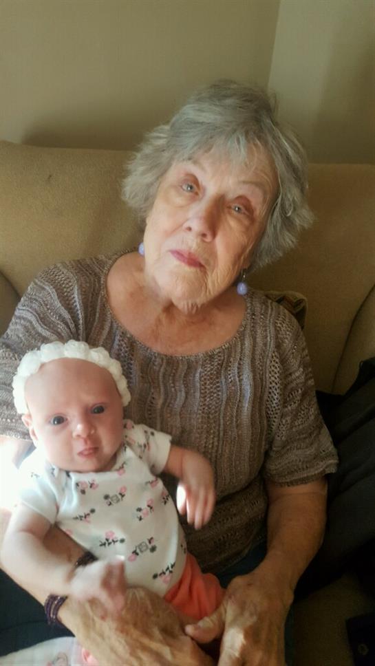 An elderly woman with gray hair holds a baby doll on her couch, enjoying the moment at home.