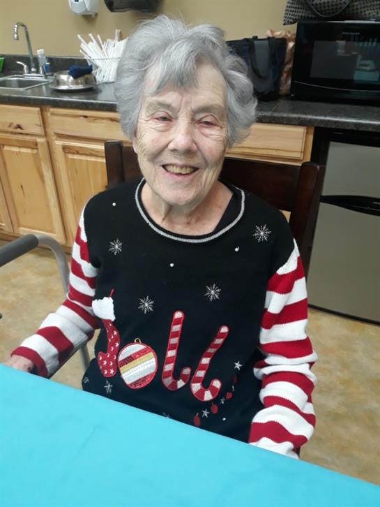 Smiling elderly woman wearing a cheerful holiday sweater participates in seasonal crafting.