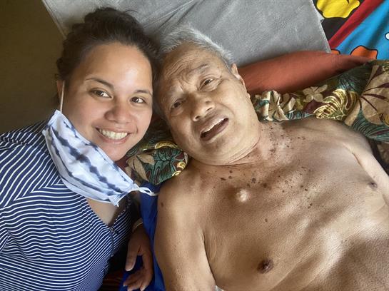 A caregiver smiles while sitting next to an elderly man, sharing a joyful moment indoors.