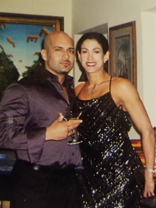 A couple dressed elegantly attends a lively gathering while holding drinks and smiling.