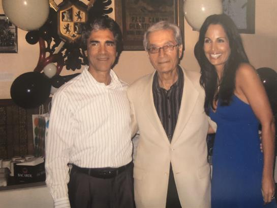 Three individuals pose together at a joyful celebration with balloons and a decorated backdrop.