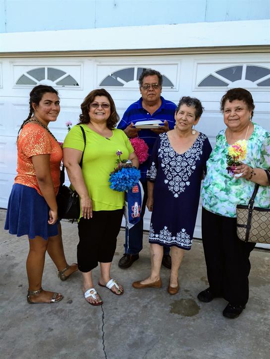 Five relatives stand together outside a garage, sharing smiles and holding items.