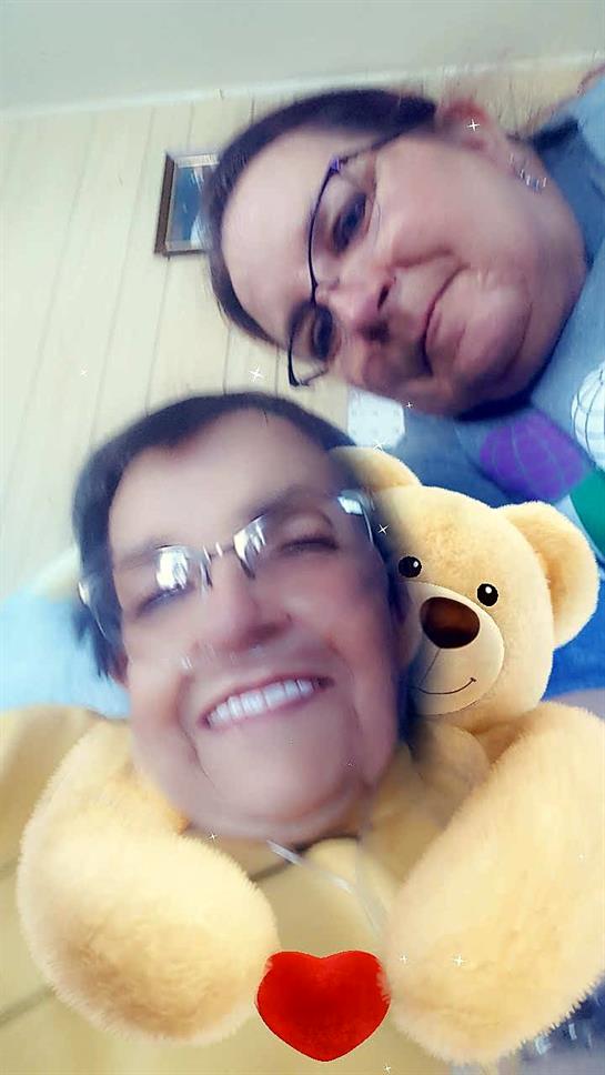 Two adults smile with a teddy bear in a cozy indoor setting.