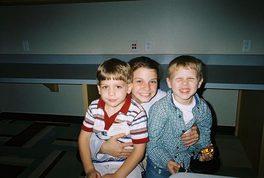 Three kids show big smiles while sitting side by side, enjoying their time together indoors.