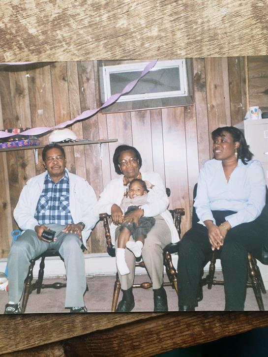 Four adults and a child laugh together in a cozy, warmly decorated living room.