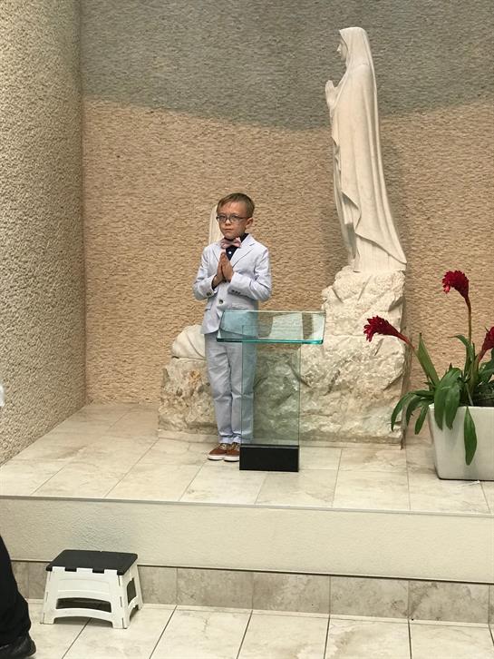 A young boy stands at a podium in a church, offering a sincere speech with prayerful hands.