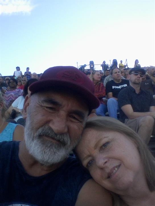 A couple smiles and leans into each other while enjoying an outdoor event surrounded by spectators.