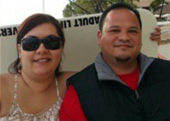 A couple stands together, both wearing sunglasses and smiling in a warm, outdoor environment.