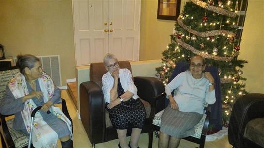 Three women chat comfortably in chairs surrounded by holiday decorations and a tree.
