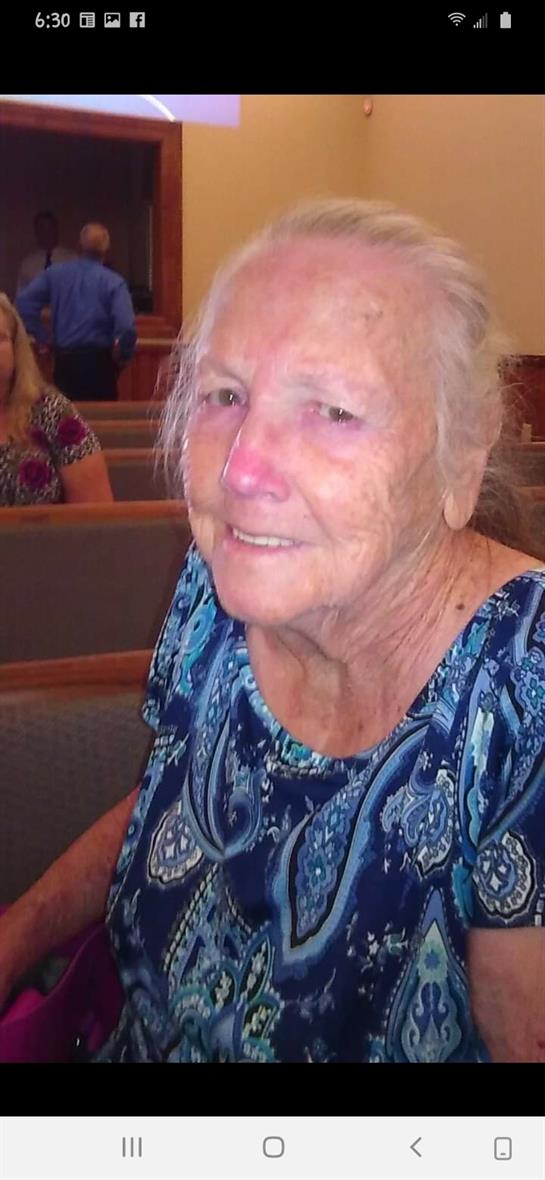 A joyful elderly woman is seated inside a church, enjoying a community event with others.