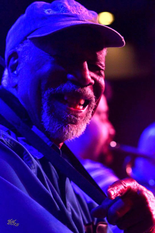 An enthusiastic musician plays a guitar on stage, surrounded by colorful lights and cheering crowd.