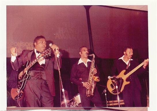 Three musicians perform for a lively audience in a vibrant club.