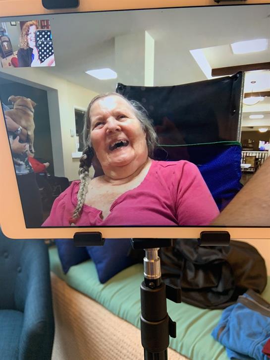 Elderly woman smiles widely as she admires herself in a mirror at a community gathering.