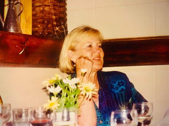 A blonde woman sits at a table, deep in thought, surrounded by flowers.