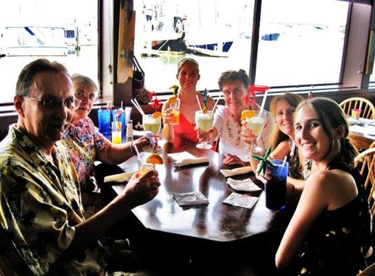 Friends enjoy colorful drinks and smiles at a waterside restaurant.