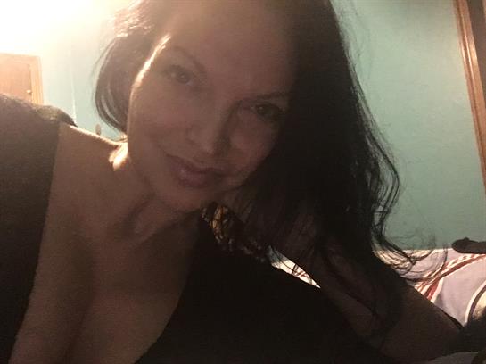 A woman enjoys a relaxed moment at home, smiling warmly while posing playfully, hair flowing freely.