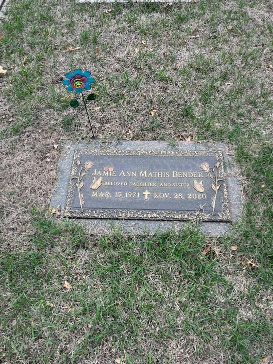 A gravestone marking the resting place of Jamie Ann Mathis Bender, surrounded by grass and a flower.