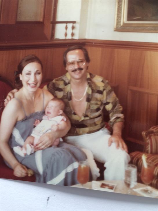 A couple poses happily with their infant in a cozy restaurant setting, surrounded by wood decor.