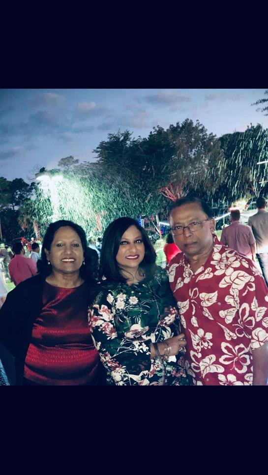 Three friends smile at a lively park gathering with festive lights.