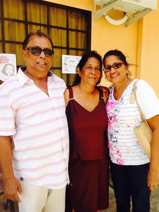 Three people smile warmly together in front of a bright orange wall, enjoying a joyful moment.