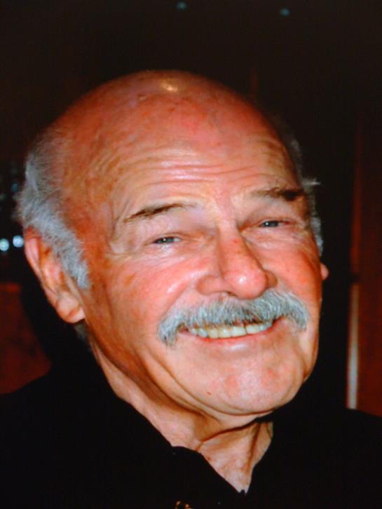 An elderly man with a friendly smile is captured in a relaxed indoor environment, radiating warmth.