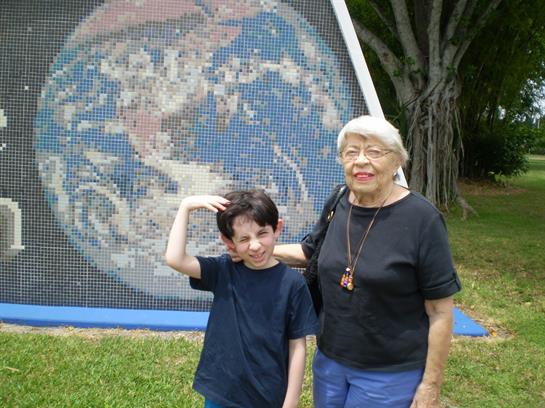 Grandmother and grandson share a joyful moment near a colorful mosaic mural of Earth in a park.