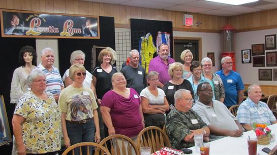 A diverse group of adults poses happily at a community event in a vibrant hall setting.