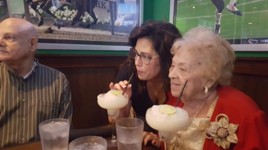 Two women and a man savoring cocktails while celebrating at a busy eatery with cheerful vibes.