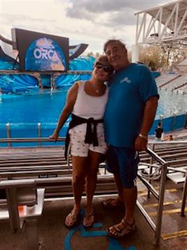A couple smiles together in front of a large stage at a marine park, enjoying their day out.