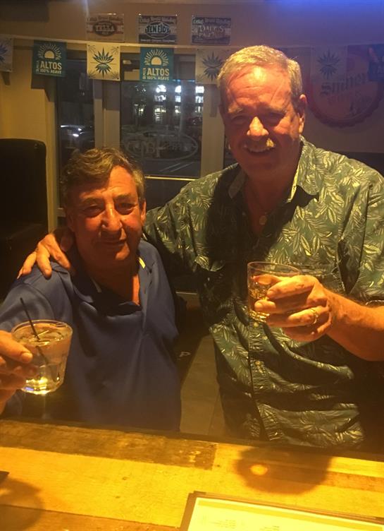 Two men are toasting with their glasses, enjoying a night out at a bar.