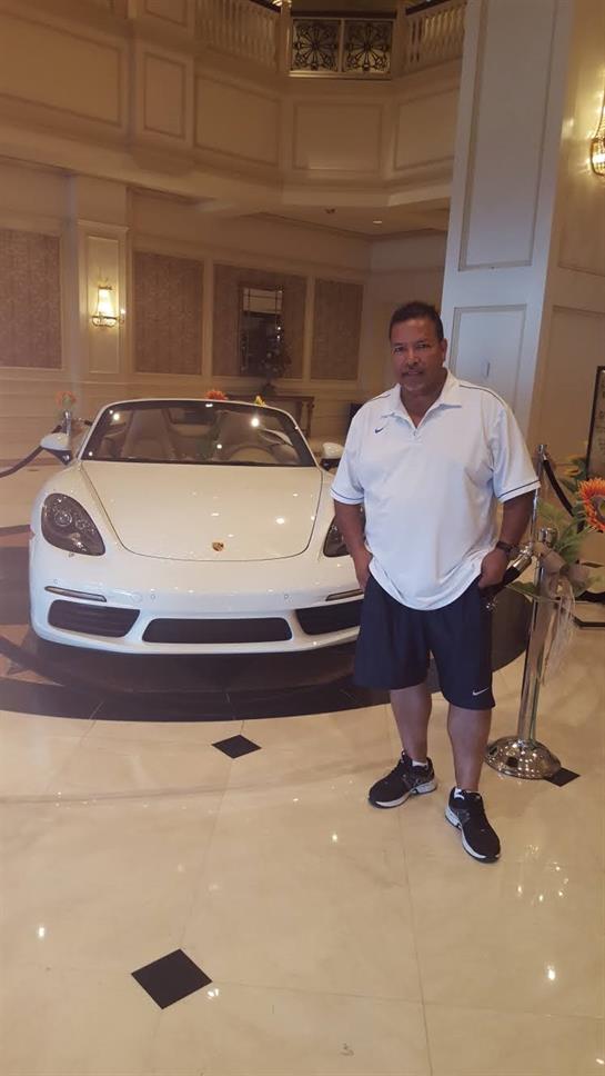 A man stands confidently next to a white sports car in an elegant hotel lobby, showcasing luxury.