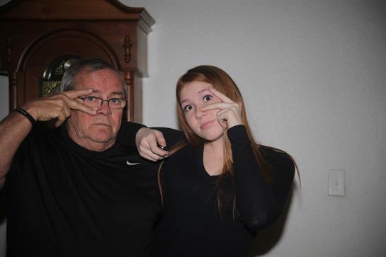 Grandfather and granddaughter pose for a lighthearted moment, making funny faces together.