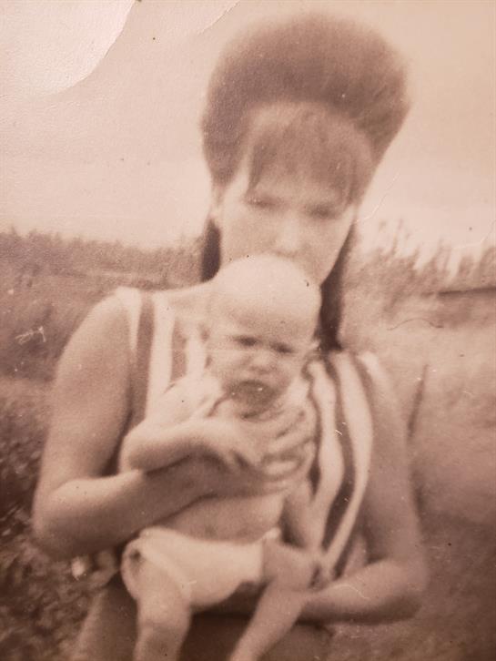 A woman lovingly holds a baby in a natural outdoor setting, radiating warmth and care.