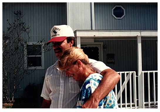 A man and woman share an affectionate moment outside their house, enjoying a warm day together.