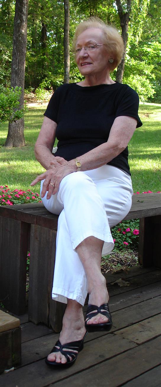 Woman enjoys a sunny afternoon in a garden, relaxing on a wooden bench with flowers nearby.