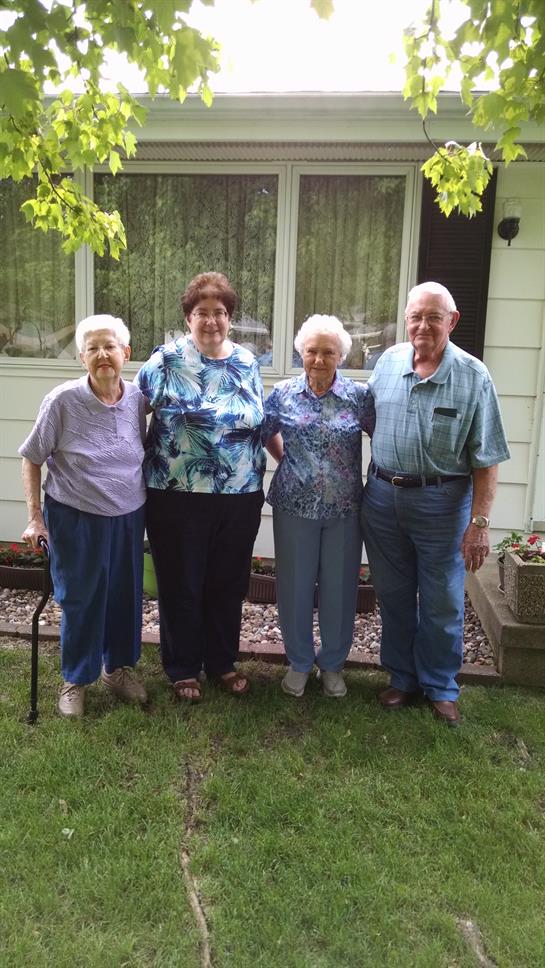 Four seniors pose together happily outside a home on a sunny afternoon, showcasing friendship.
