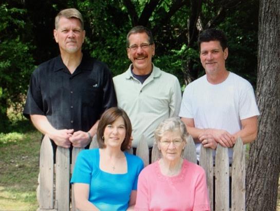 Five family members stand together in a rustic yard, enjoying their time outdoors on a sunny day.