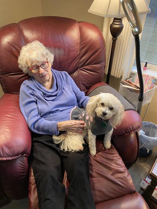 An elderly woman relaxes in a recliner while petting her small dog in a cozy room.