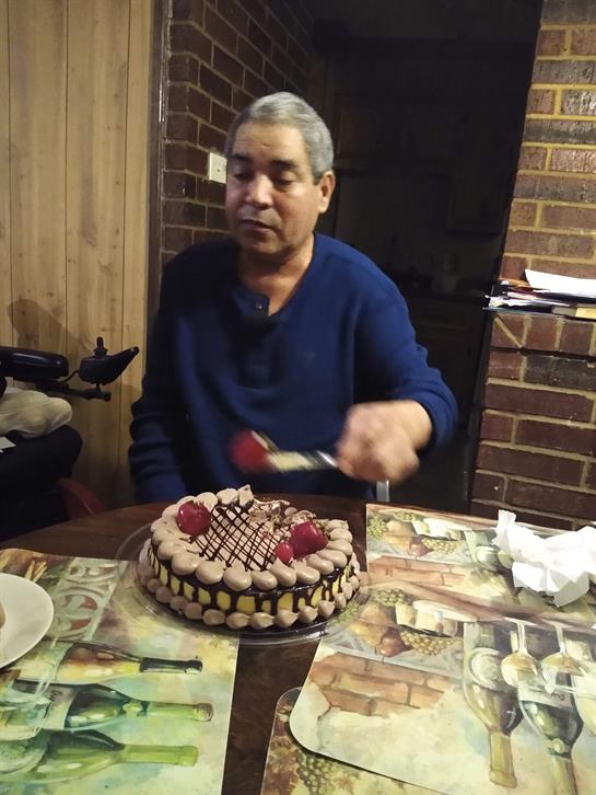 A man in a cozy setting carefully serves a chocolate cake adorned with strawberries for dessert.
