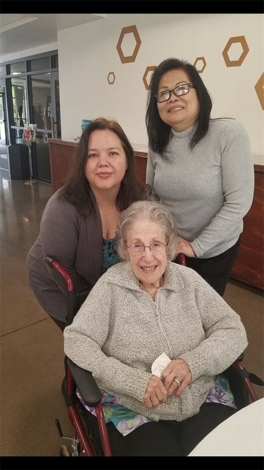 Three women share a heartfelt moment during a visit at a community center, celebrating together.